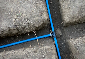 Eine Klemmverschraubung mit drei Anschlüssen verbindet PEX-Rohre in einem unterirdischen Bewässerungssystem.