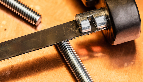 Close up on a hacksaw blade’s teeth above a cut steel screw.