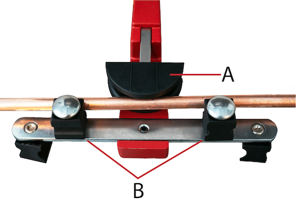 Une matrice de pliage noire (A) sur le point de presser un tuyau en laiton dans deux rouleaux fixes (B).