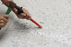 Using a masonry chisel to prepare a floor for new tiling.