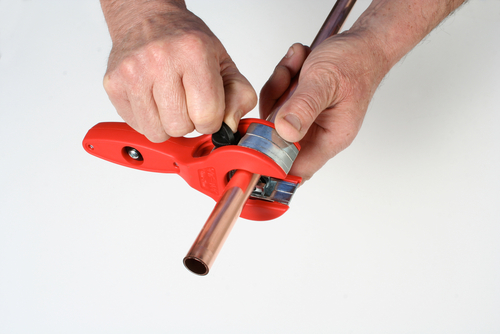 A ratchet pipe cutter cutting through copper pipe.